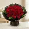Luxury red rose bouquet wrapped in translucent dark brown and black paper with fresh green foliage